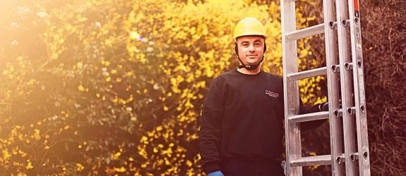 Gutter cleaner holding a ladder wearing a hard hat and bens gutters uniform