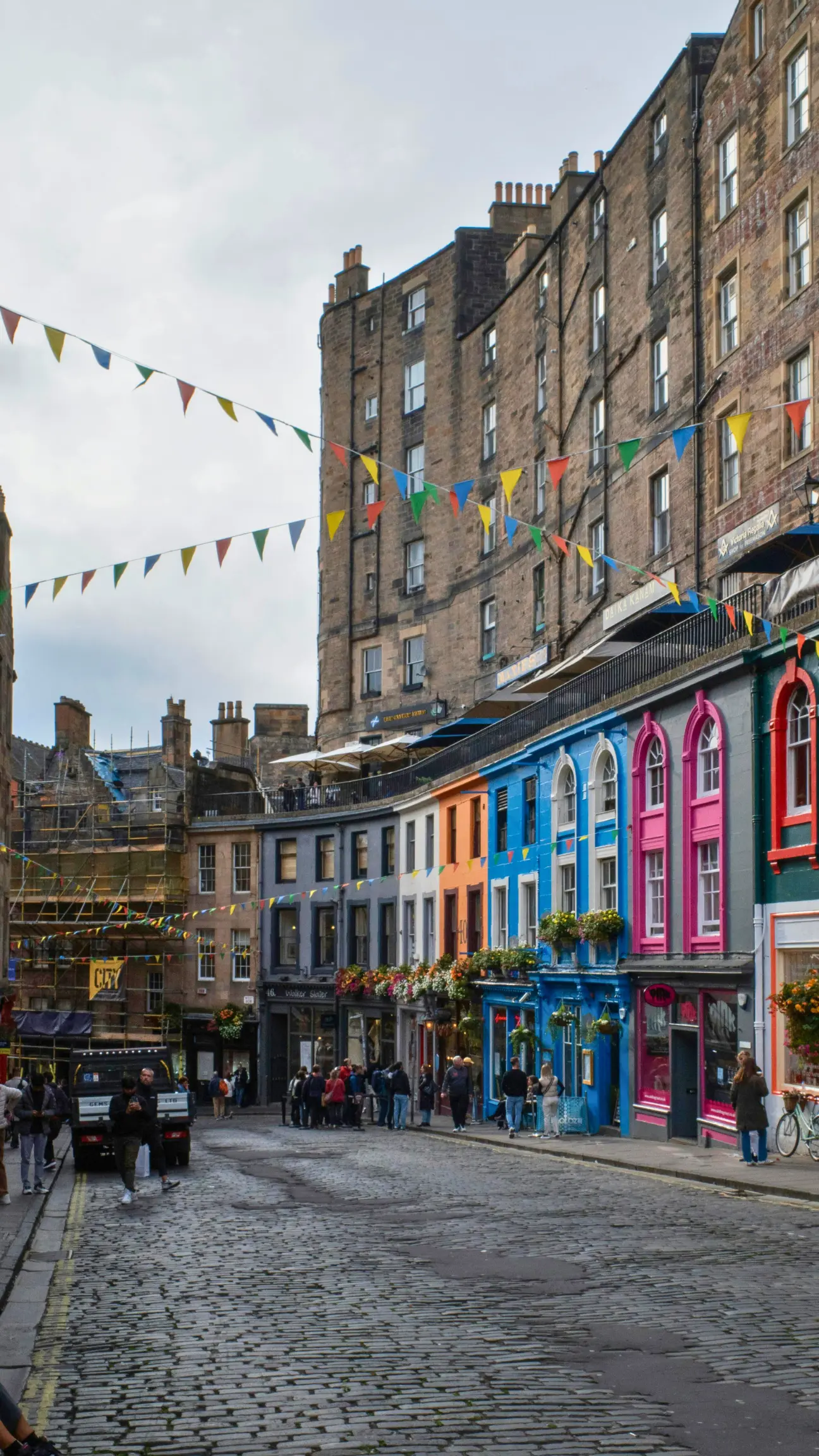 A vibrant street scene in Edinburgh with colourful buildings and hanging baskets, representing the character of local homes that benefit from regular gutter cleaning and maintenance.